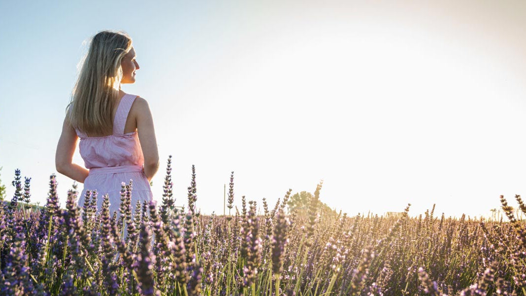 Woman in summer dress walking in a meadow in sunset