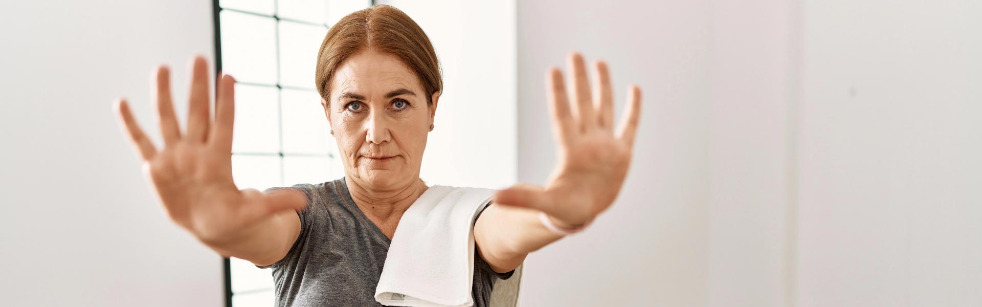 A middle aged woman holding her arms up as to stop dressed in training outfit at a gym