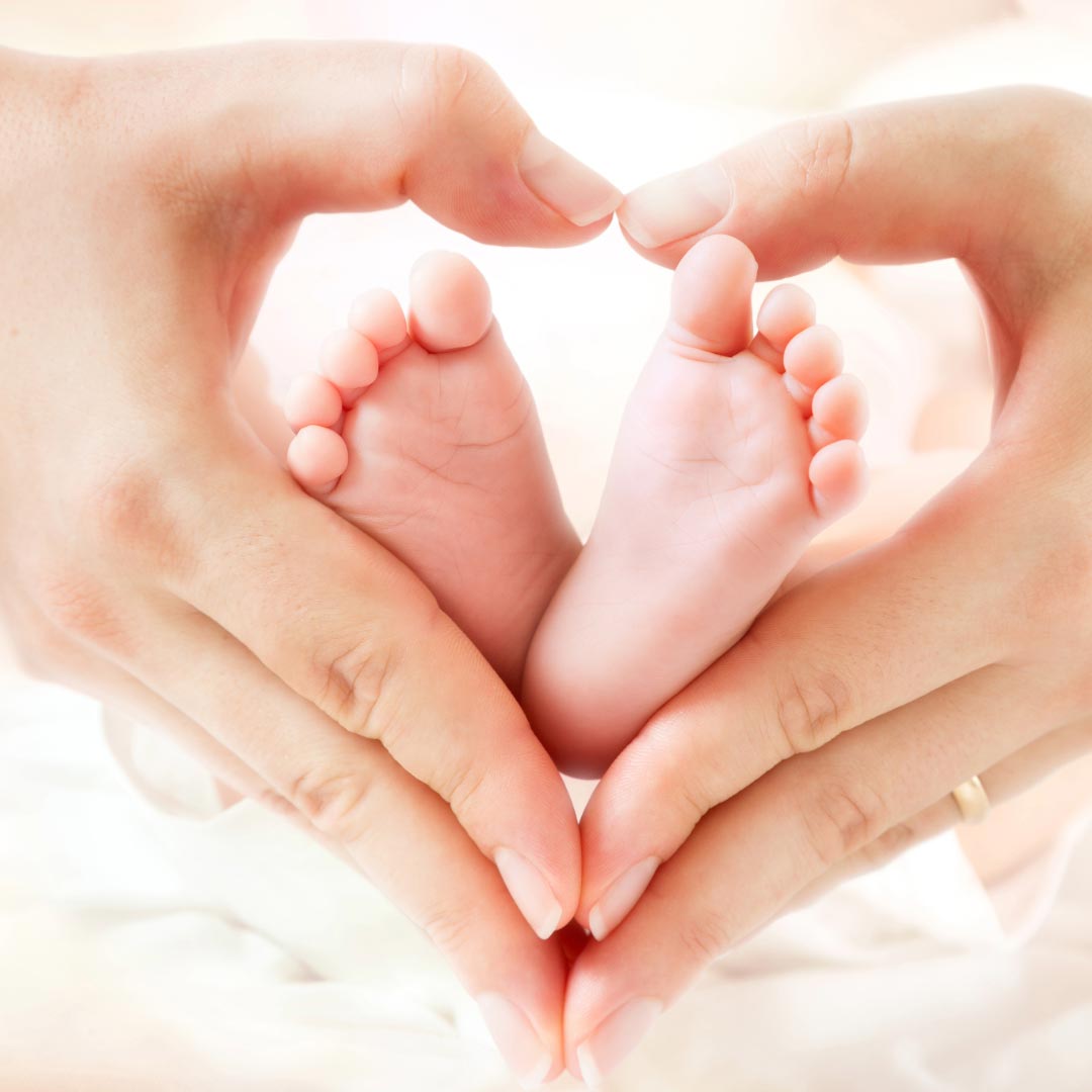 A woman's hands making a heart around baby feet
