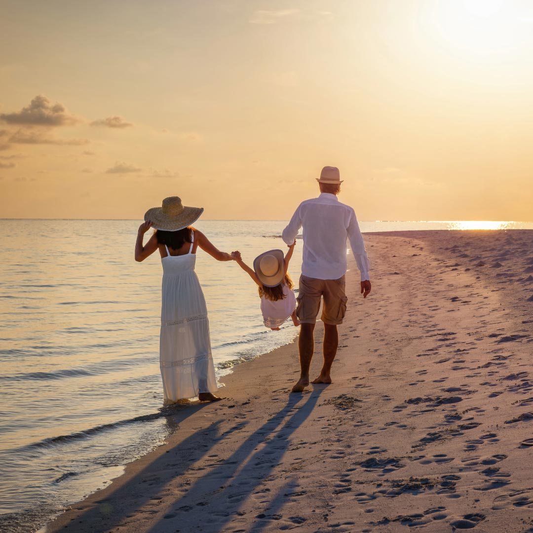 A woman and man holding a little girl between them walking on the beach in sunset