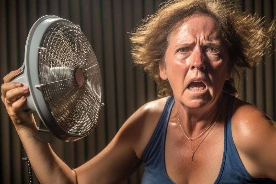A middle aged woman looking crazy from hot flashes during menopause holding a fan in her hand