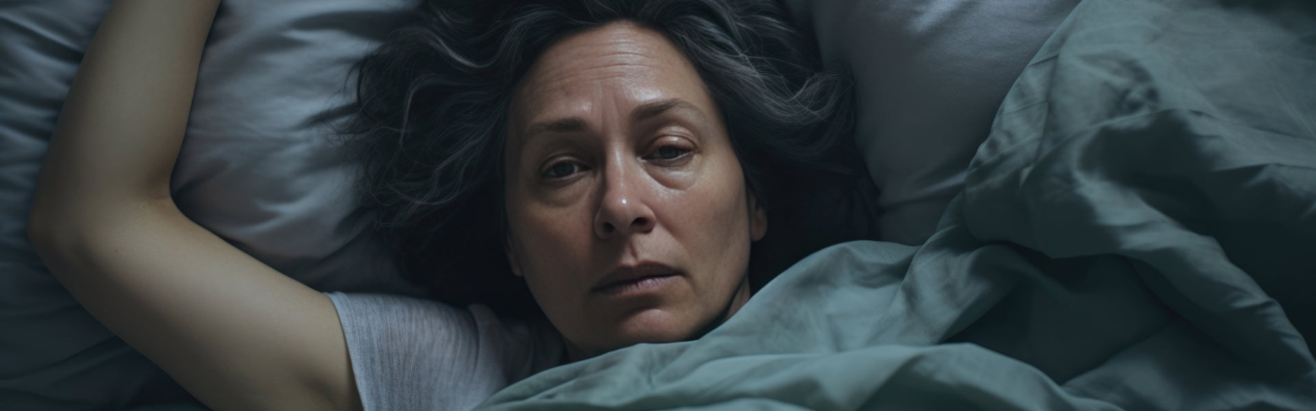 A woman laying in bed struggling to sleep and looking exhausted