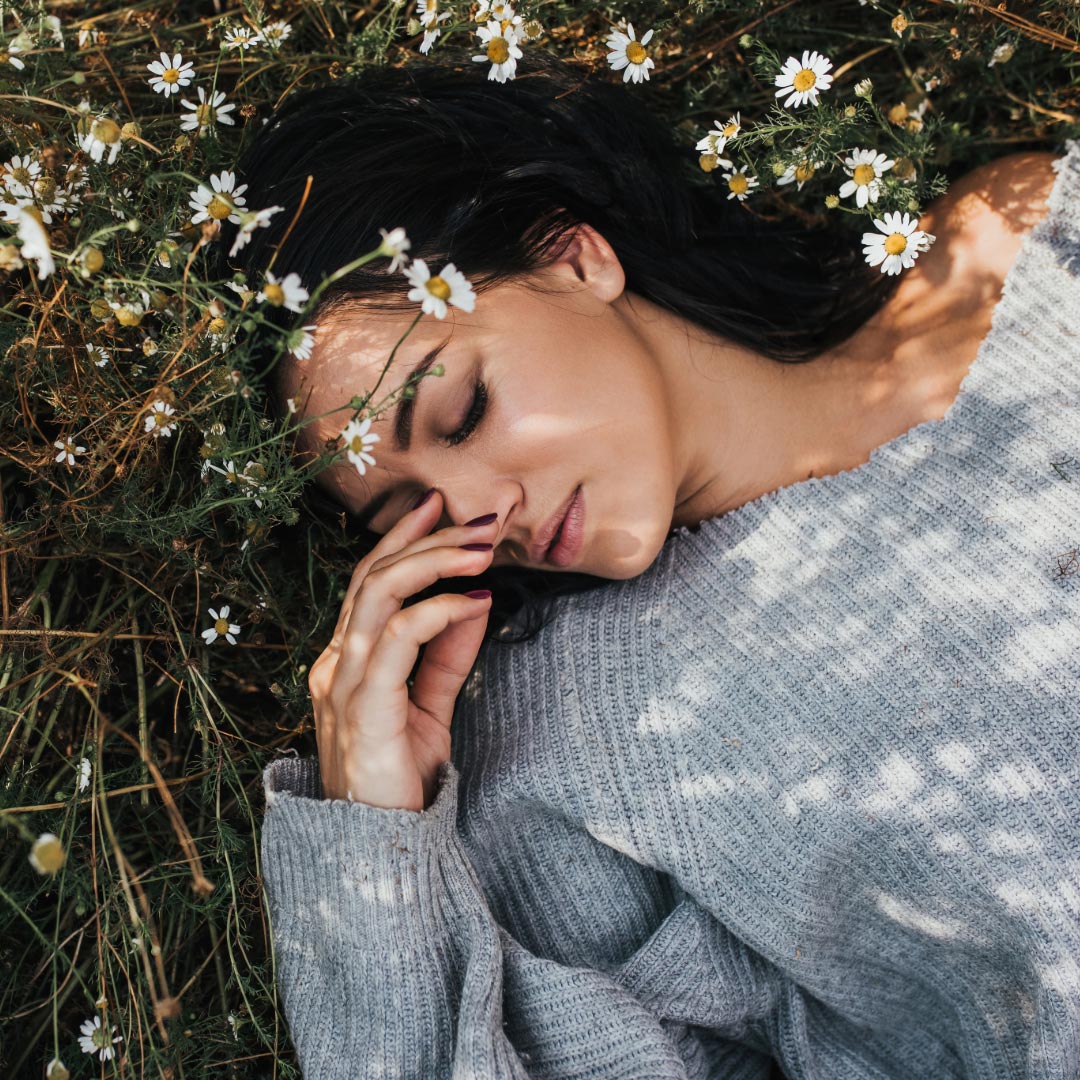A woman in a grey knitted sweater laying in a meadow with her eyes closed
