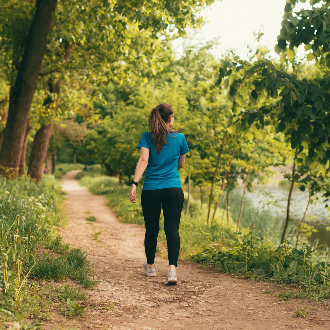 A woman in work out clothes on a path in the woods by a lake