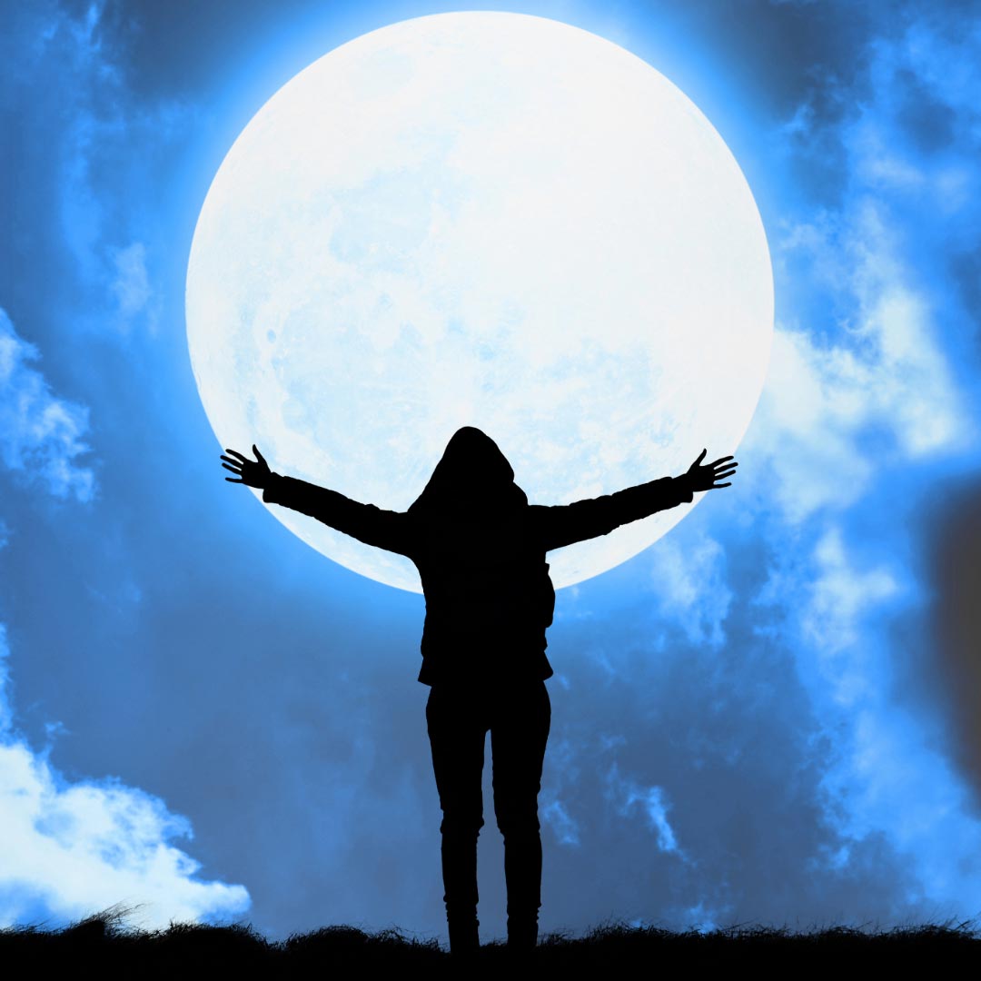 A woman standing holding her arms out like embracing the moon in the background